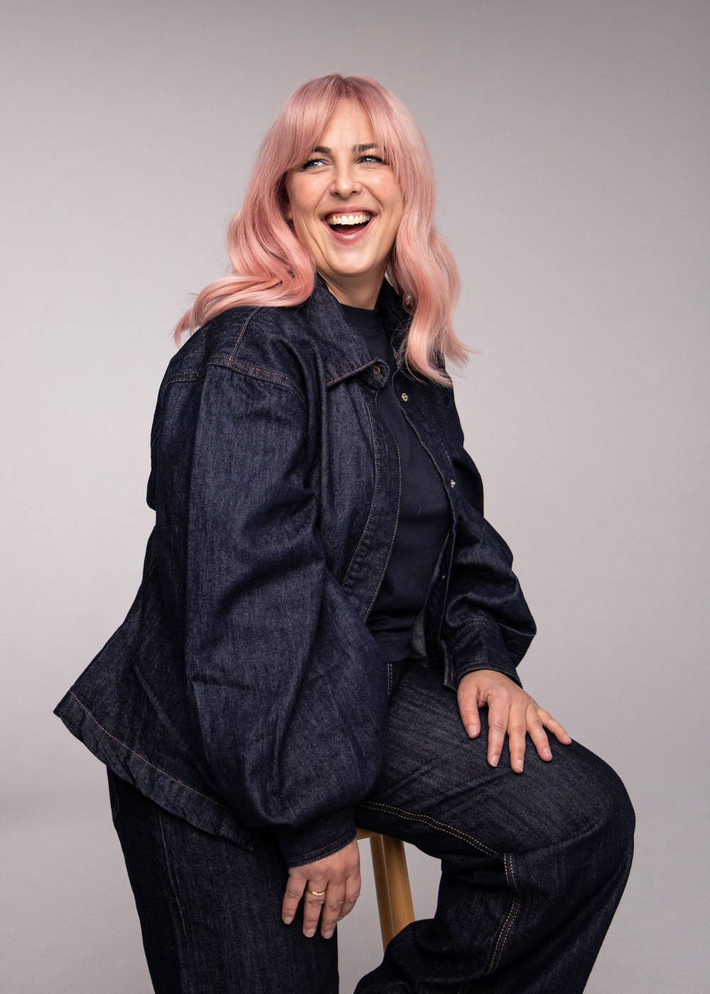 Person med puderrosa hår i mjuka längder, sittande i denimkläder mot neutral bakgrund