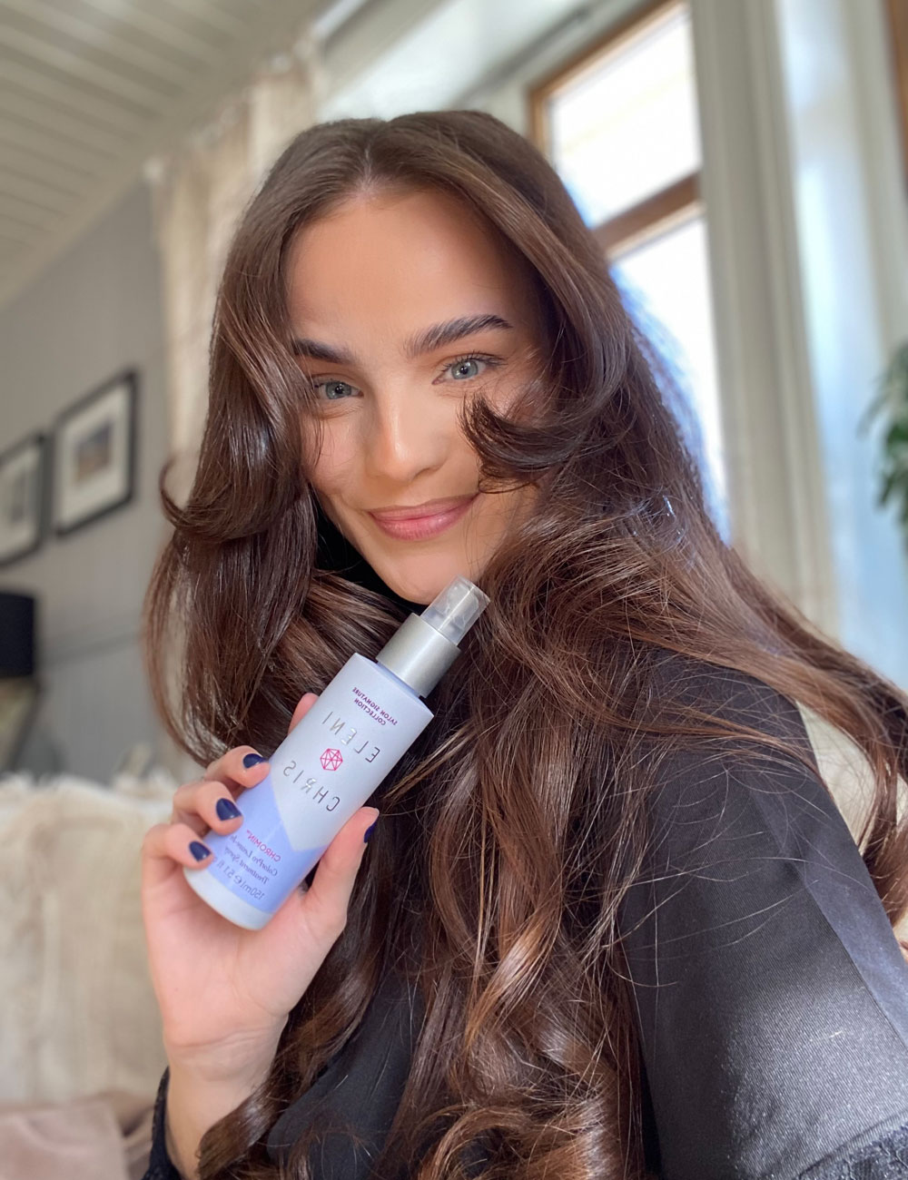 Kvinne med langt, glansfullt brunt hår som holder et hårpleieprodukt